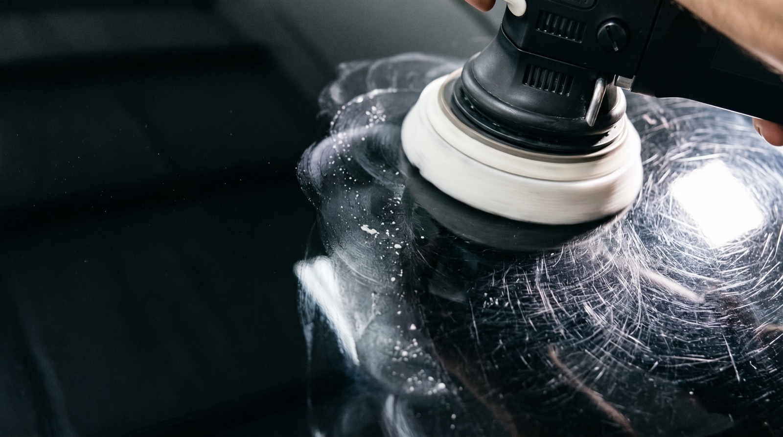 Close-up of a dual-action polisher correcting swirl marks on car paint